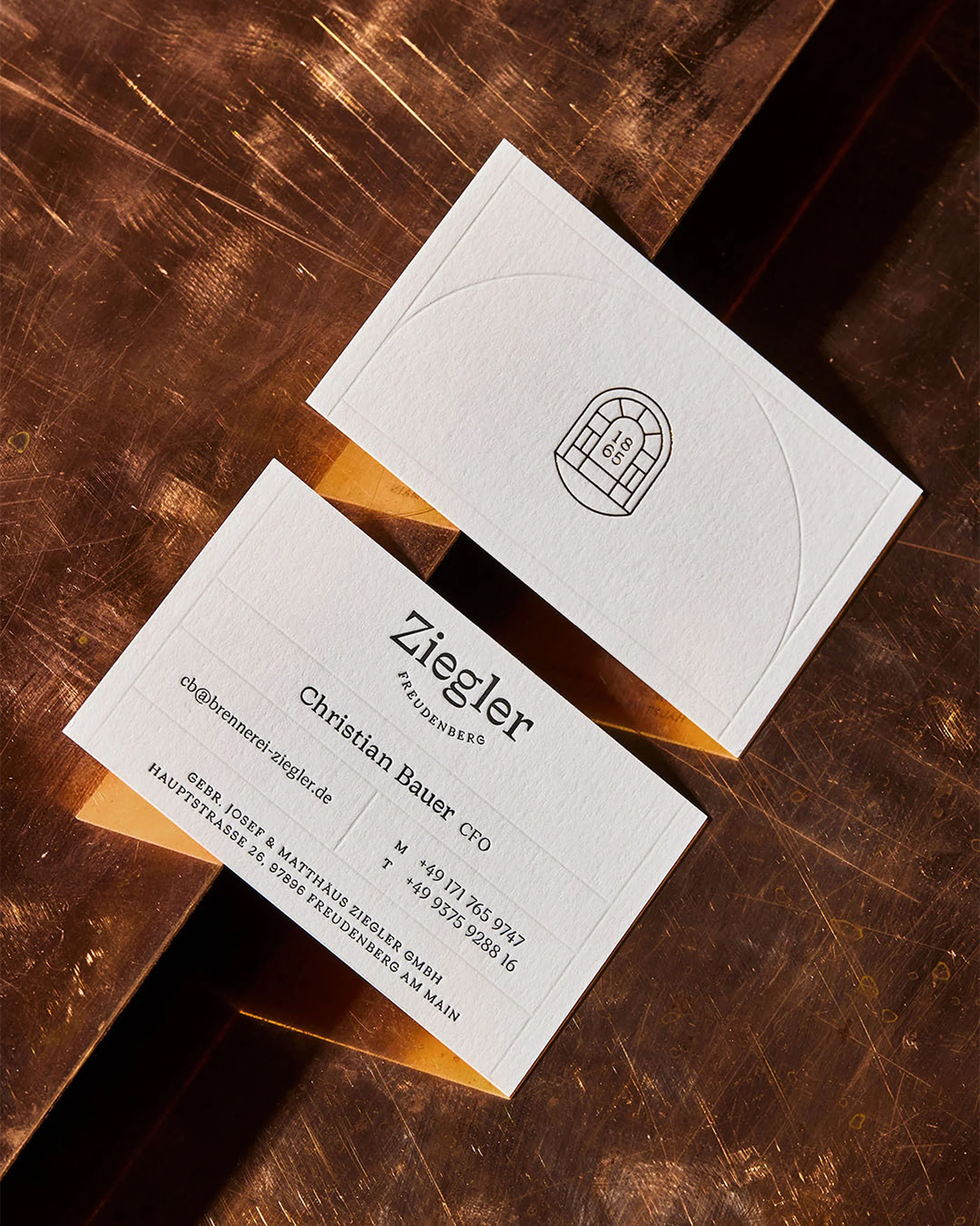 Two elegant business cards with the company Ziegler prominently displayed, resting on a textured bronze surface with soft, diffused lighting.