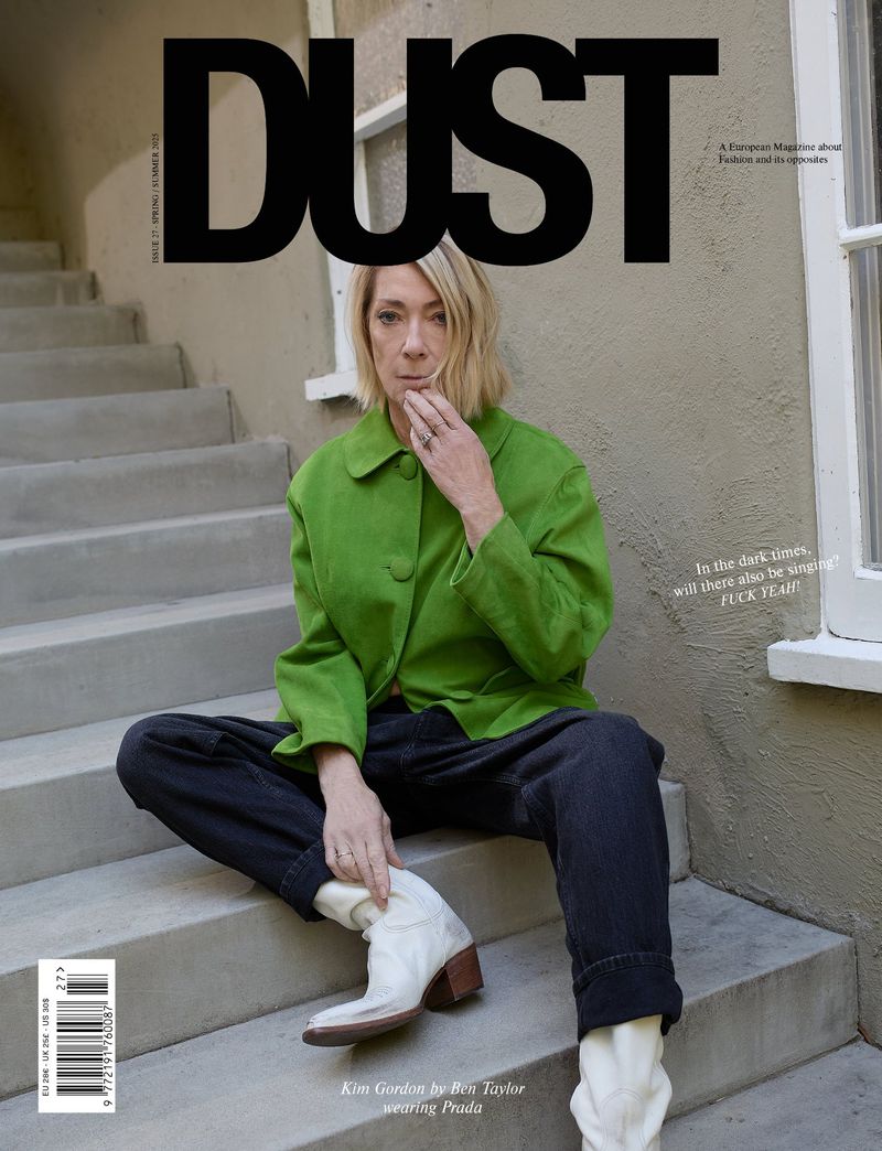 Magazine cover featuring an adult woman with blonde hair, wearing a green jacket, black pants, and white boots, sitting on concrete steps.