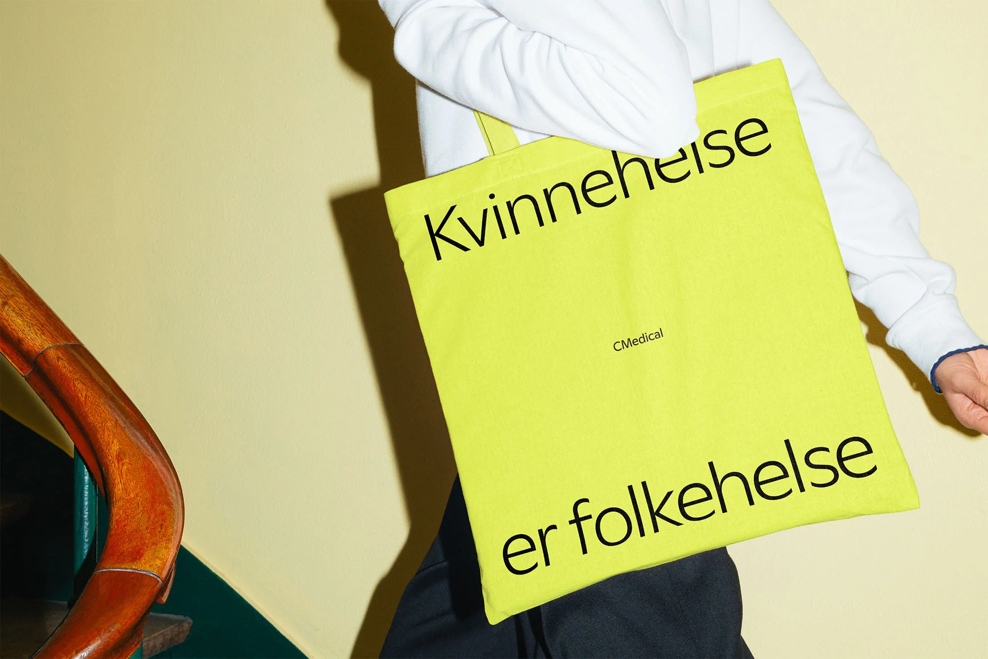 Person holds a bright yellow tote bag with the text 'Kvinnehelse er folkehelse' in black lettering against a yellow wall.