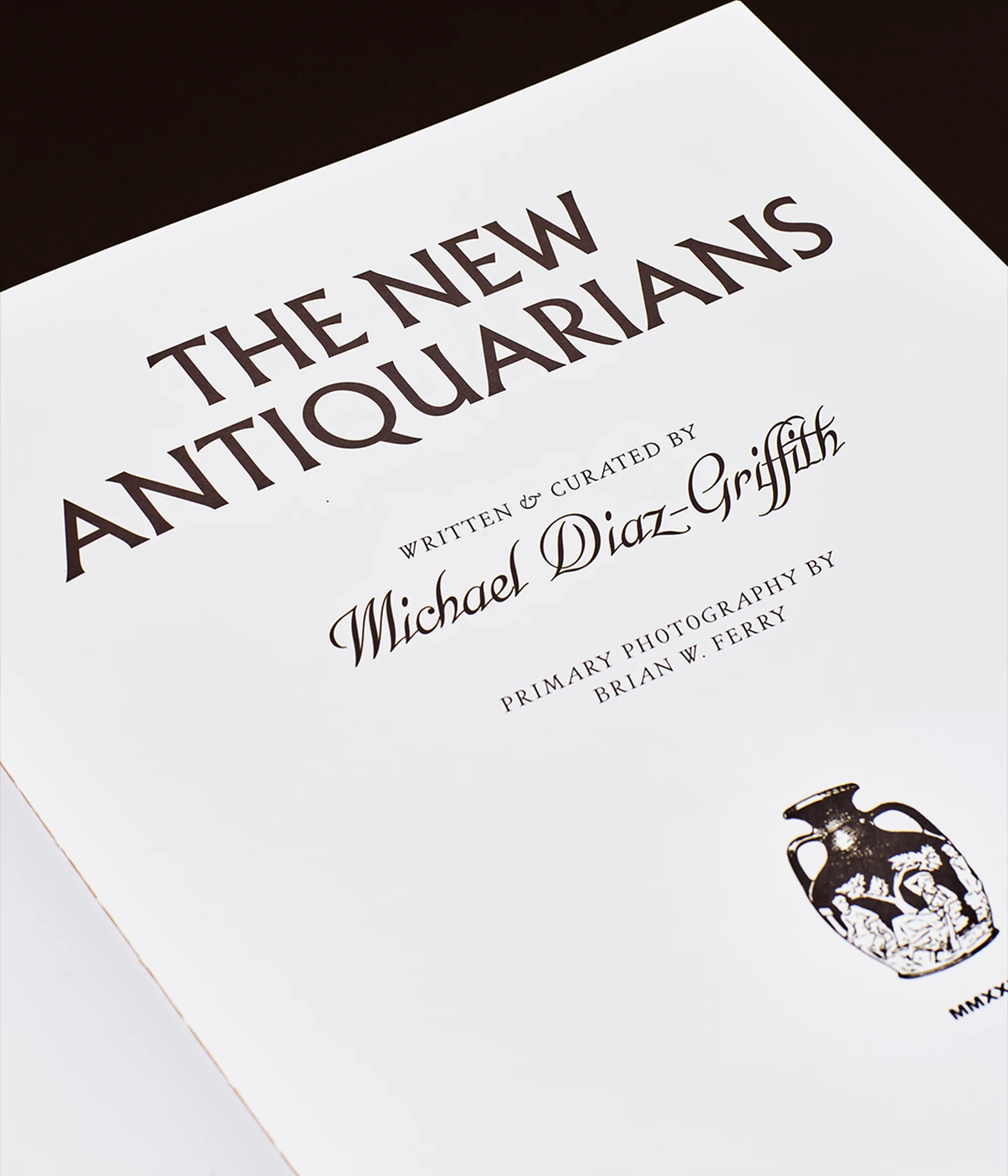 Close-up photograph of the cover of 'The New Antiquarians' book, written and curated by Michael Diaz-Griffith, with an antique vase illustration.