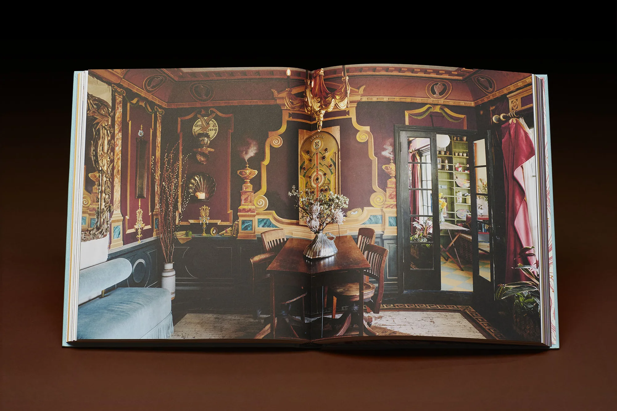 Open book displays a photograph of an ornately decorated room with dark walls, a wooden table, and chairs, illuminated by a chandelier.