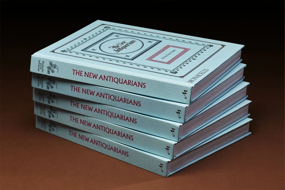 Stack of 'The New Antiquarians' books by Michael Diaz-Griffith and published by Monacelli, featuring a light blue cover with ornate design.