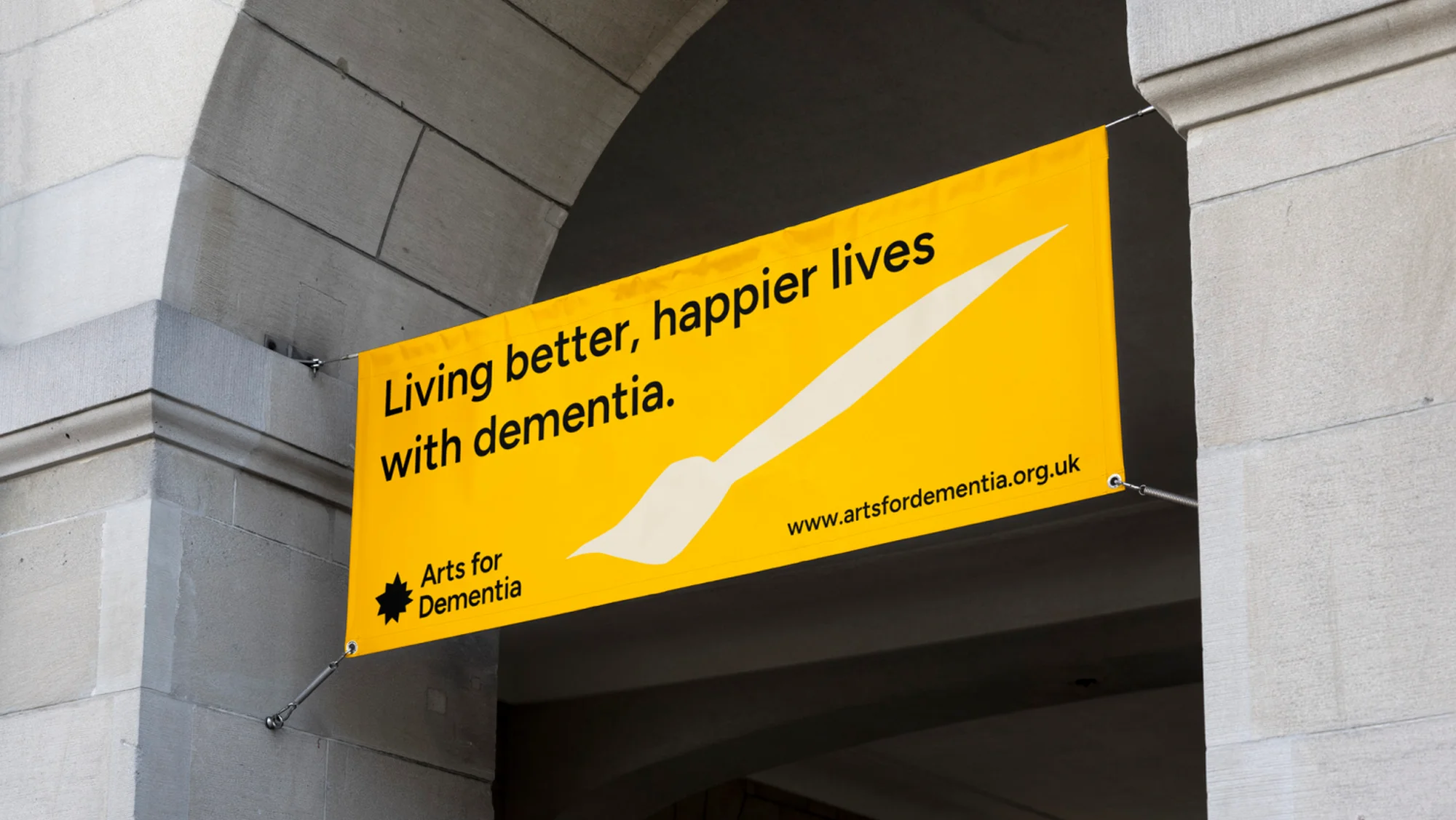 Yellow banner for Arts for Dementia featuring the slogan 'Living better, happier lives with dementia' under an arched stone structure.