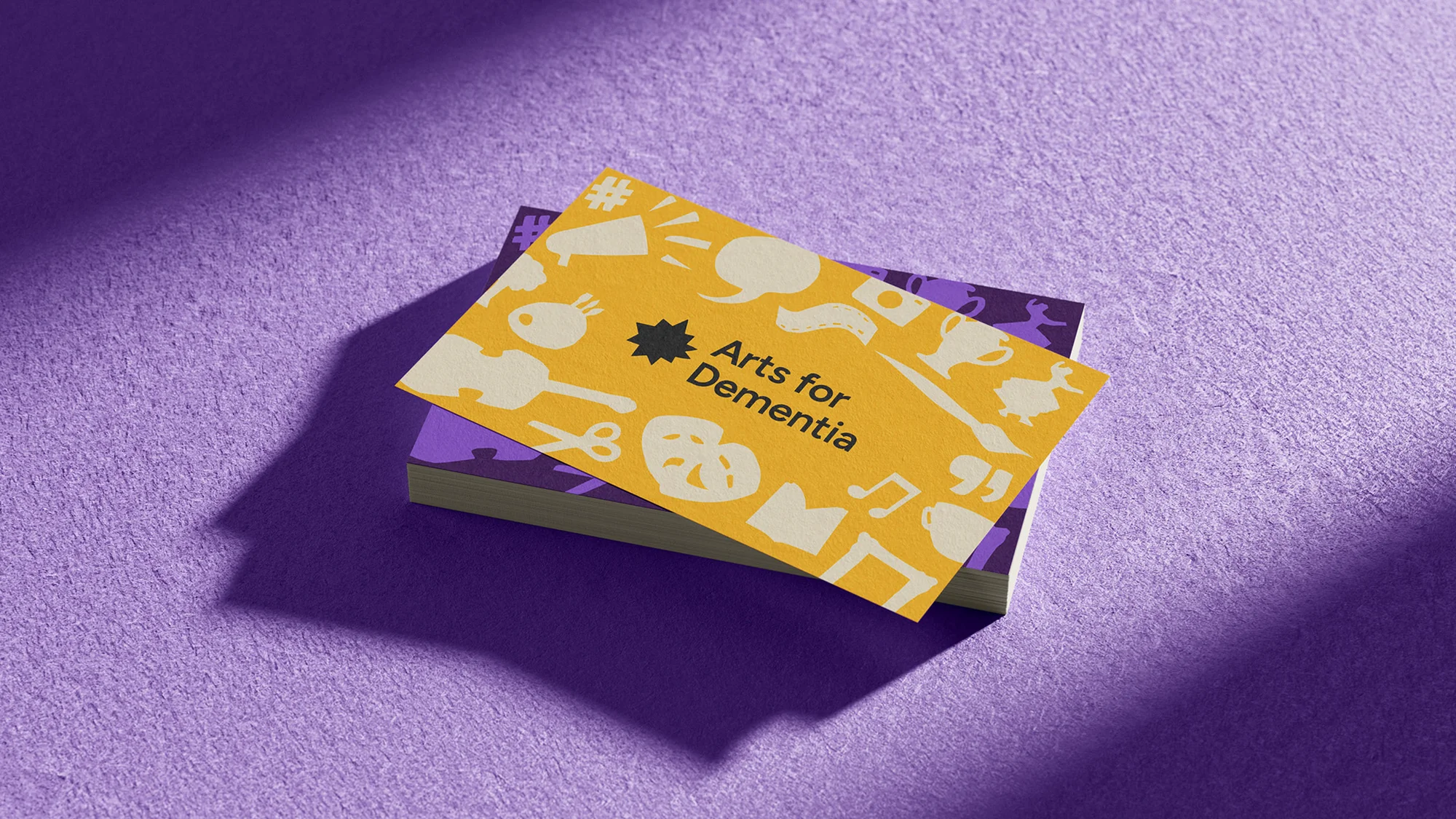 Close-up of stacked business cards with a yellow top card featuring arts-related icons on a purple textured surface with a soft shadow.