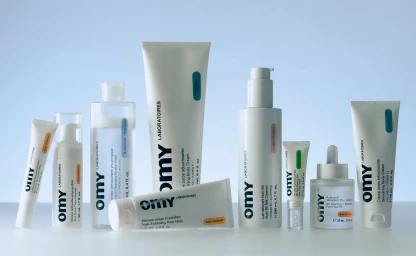 Collection of Omy skincare bottles and tubes arranged on a smooth white surface against a light blue backdrop.