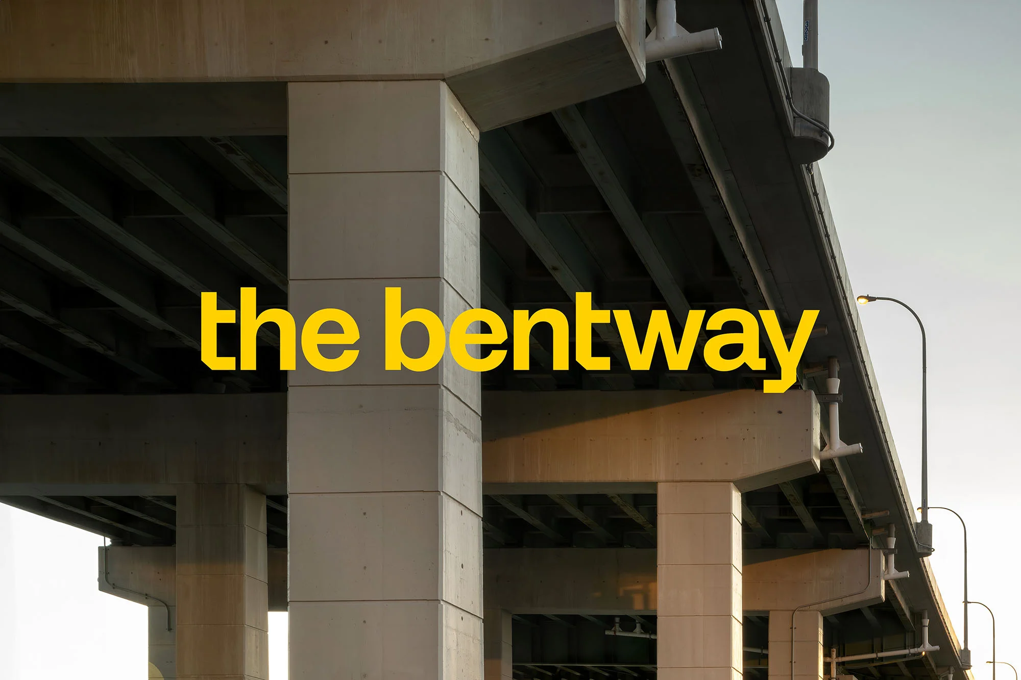 Concrete pillars supporting an elevated structure with 'the bentway' text overlayed, viewed from a low angle on a bright day.