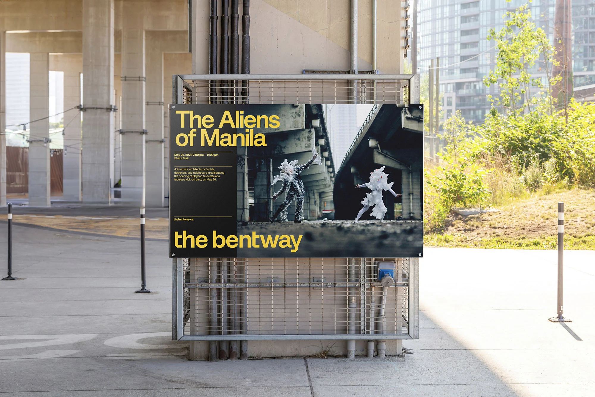 Outdoor poster for 'The Aliens of Manila' art event featuring costumed performers, set against an urban concrete landscape and lush greenery.