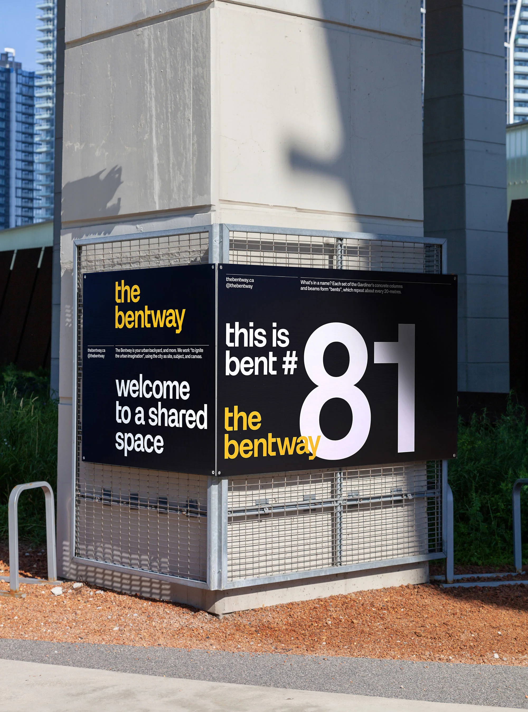 Outdoor view of a signage display for The Bentway, welcoming visitors to a shared space, with modern architecture and greenery in the background.