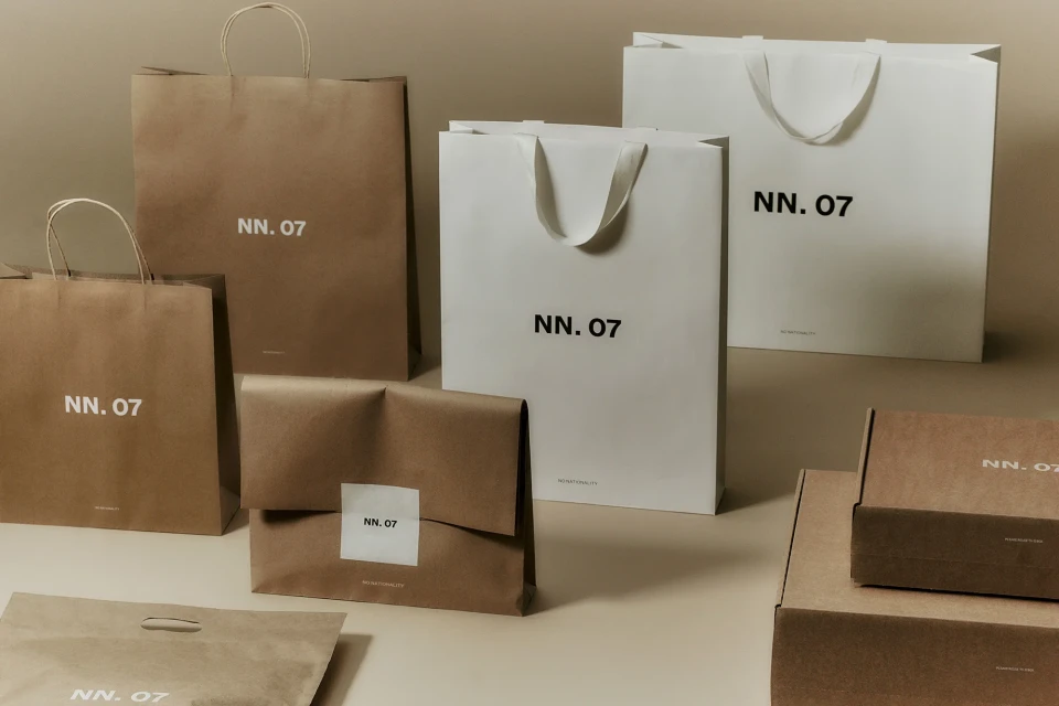 Several brown and white shopping bags and boxes with the brand NN. 07 are displayed on a neutral background, creating a simple and modern layout.