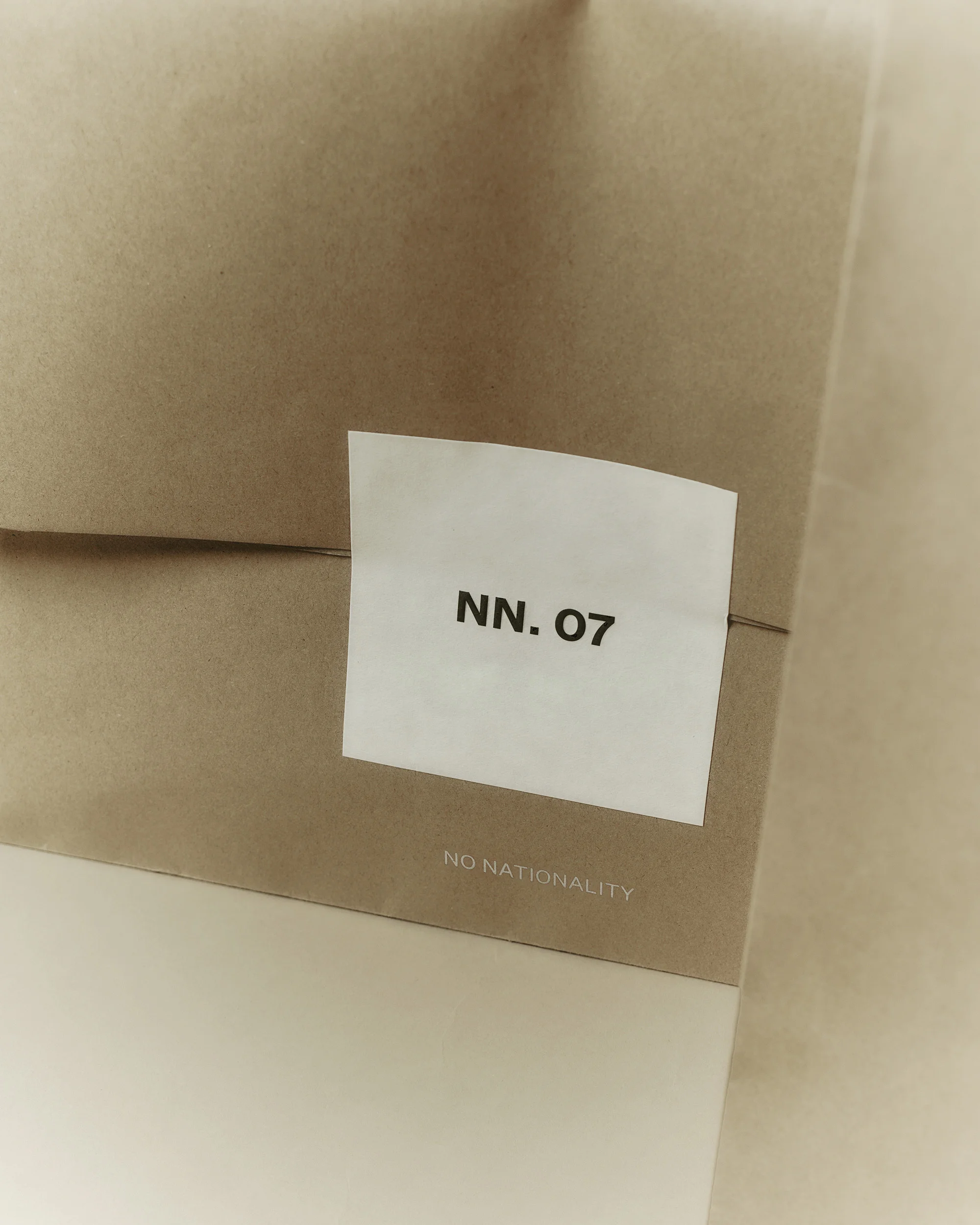 Close-up of a brown paper bag with a white label reading 'NN. 07' and the text 'NO NATIONALITY' printed at the bottom.
