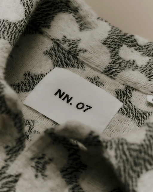 Close-up of a white and grey patterned shirt with a tag reading 'NN. 07,' highlighting fabric details and brand label.