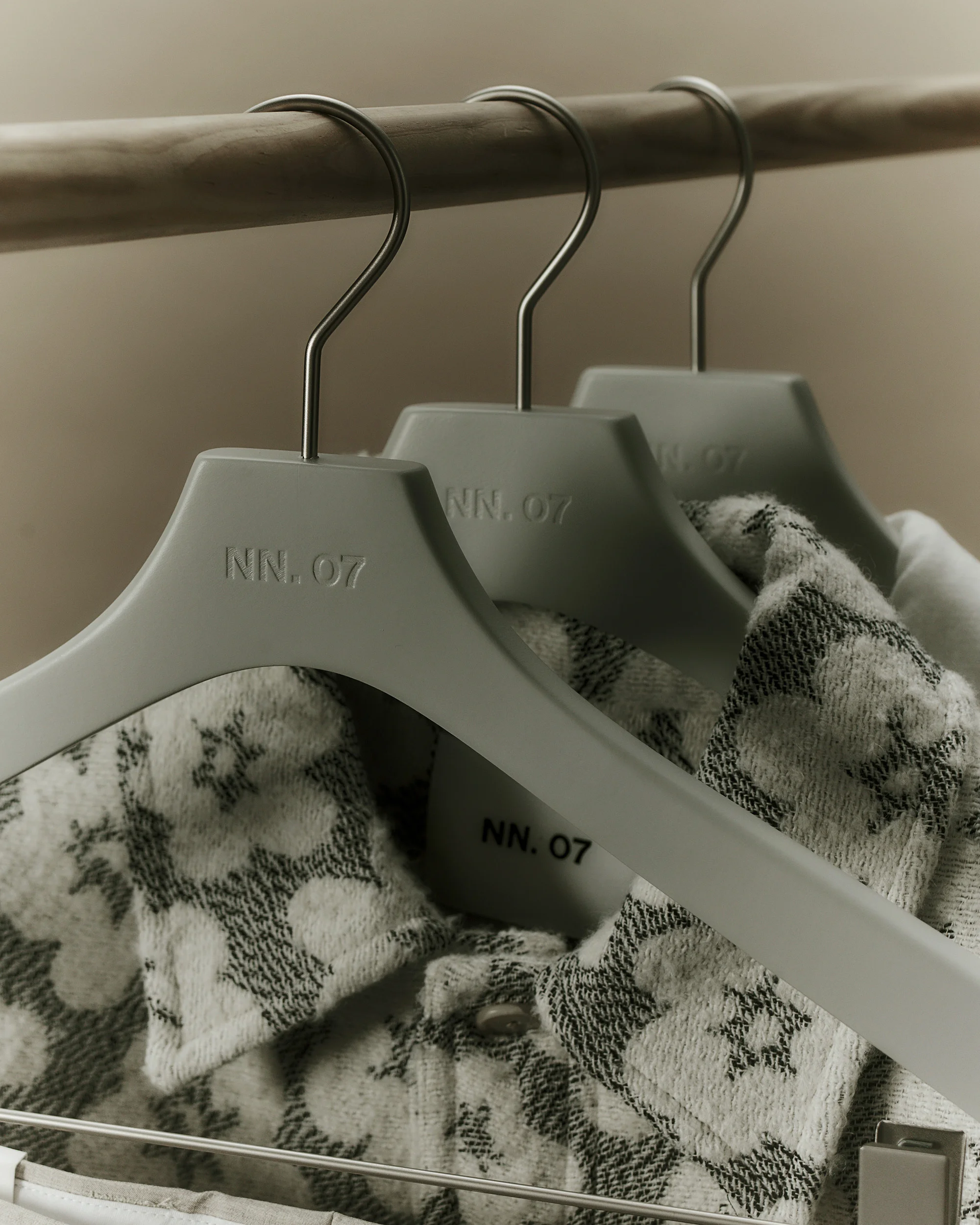 Three gray hangers with shirts hang on a wooden rod. Neutral background, studio product shot.