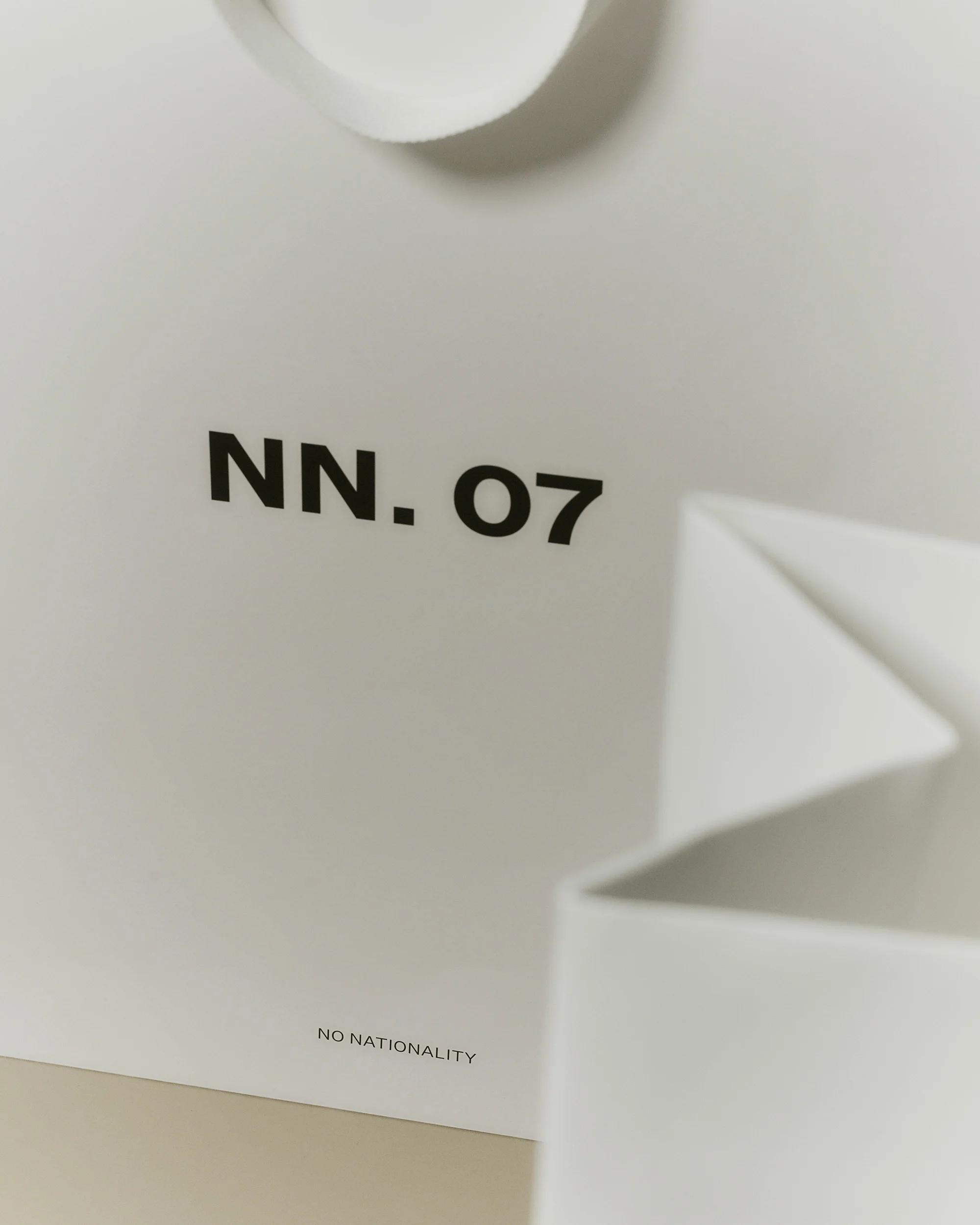 Close-up of a white paper shopping bag with the text "NN. 07" and "NO NATIONALITY" printed in black, emphasizing minimalist design.