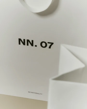Close-up of a white paper shopping bag with the text "NN. 07" and "NO NATIONALITY" printed in black, emphasizing minimalist design.