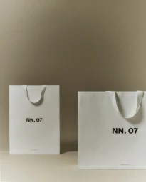 Two white paper shopping bags featuring the NN.07 logo set against a neutral beige background.