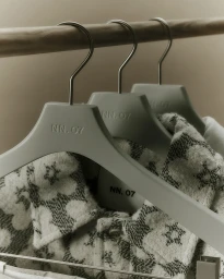 Three branded clothes hangers holding patterned garments on a wooden clothing rail in a minimalist setting for NN07.