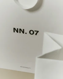 White shopping bag featuring NN.07 brand logo with folded white paper edges in the foreground