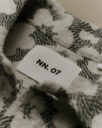 Close-up macro shot of a patterned fabric collar featuring a white clothing label with black text NN.07.