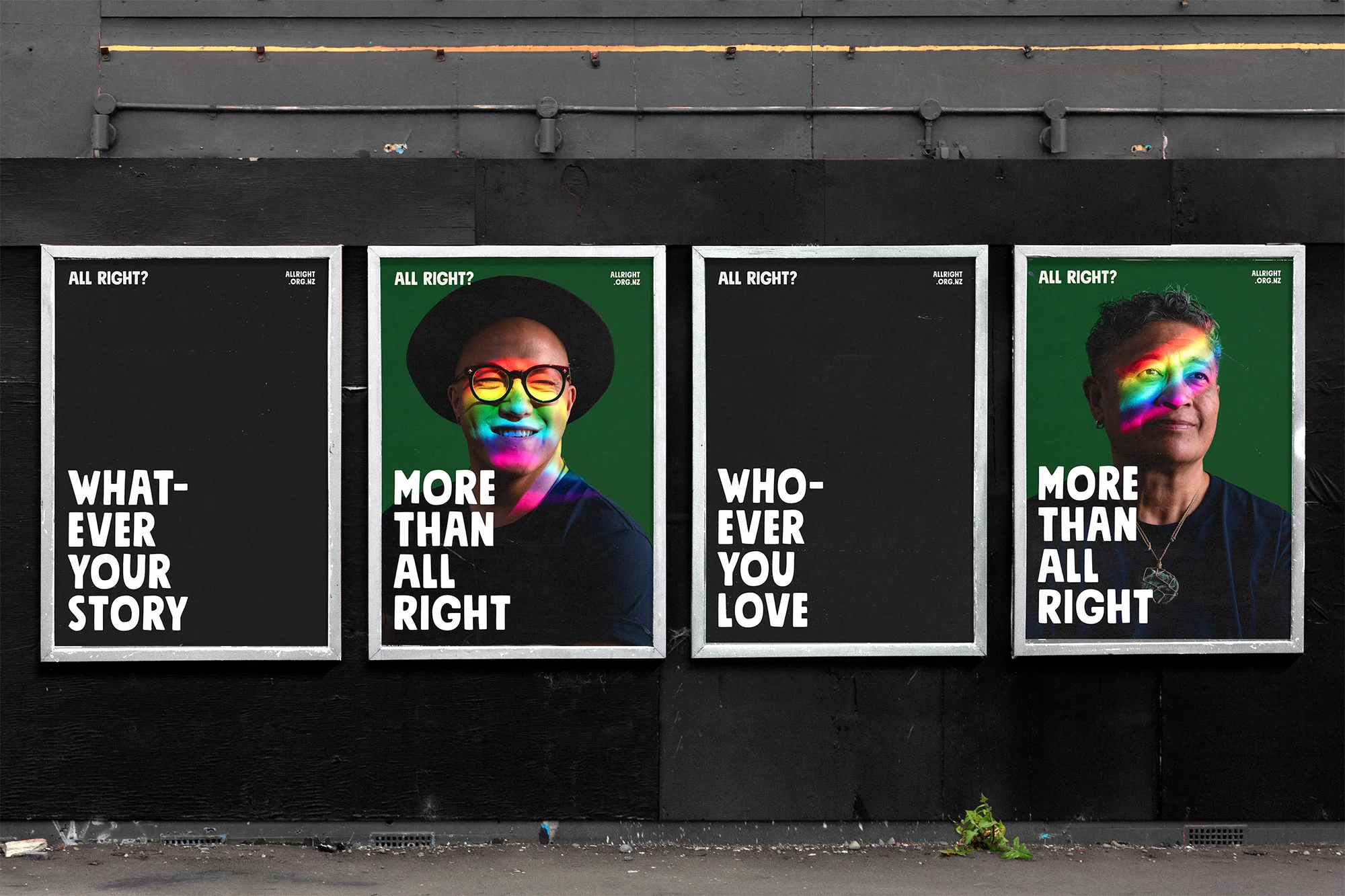 Eye-level outdoor shot of four framed posters mounted on a black wall, each featuring LGBTQ+ positive messages and portrait photography.