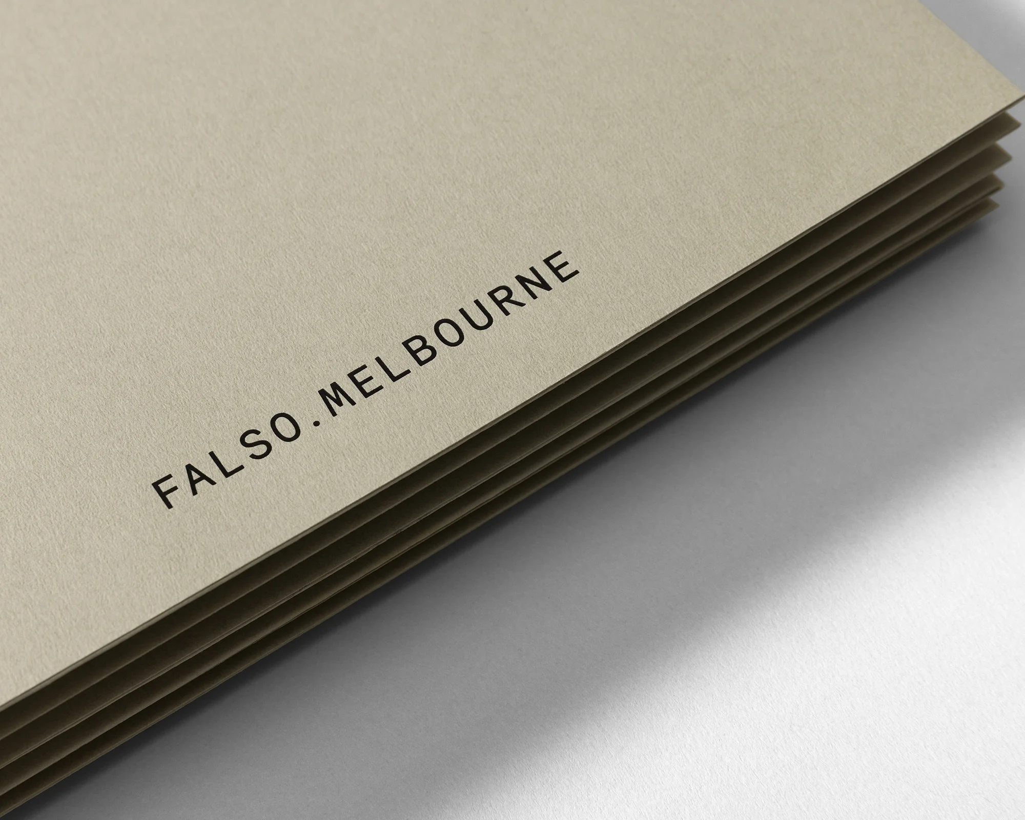 Close-up of stacked cream-colored sheets of paper with the black text “FALSO.MELBOURNE” printed on them in a simple sans-serif font.