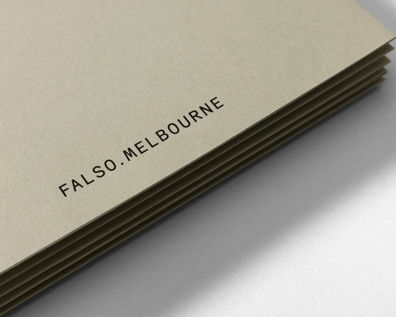Close-up of stacked cream-colored sheets of paper with the black text “FALSO.MELBOURNE” printed on them in a simple sans-serif font.