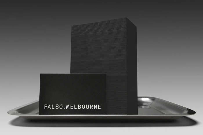 Black business card and tall stack of black paper on a shiny silver metal tray against a grey background.