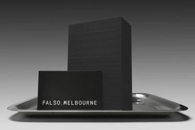 Black business card and tall stack of black paper on a shiny silver metal tray against a grey background.