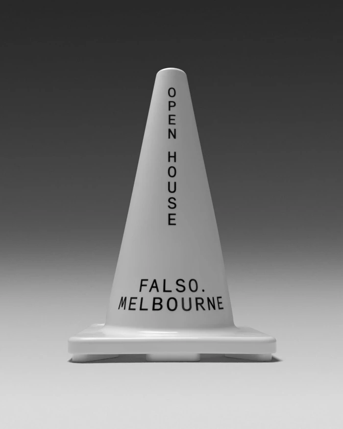 A smooth white traffic cone featuring printed black lettering reading OPEN HOUSE and FALSO MELBOURNE against a grey gradient studio background.