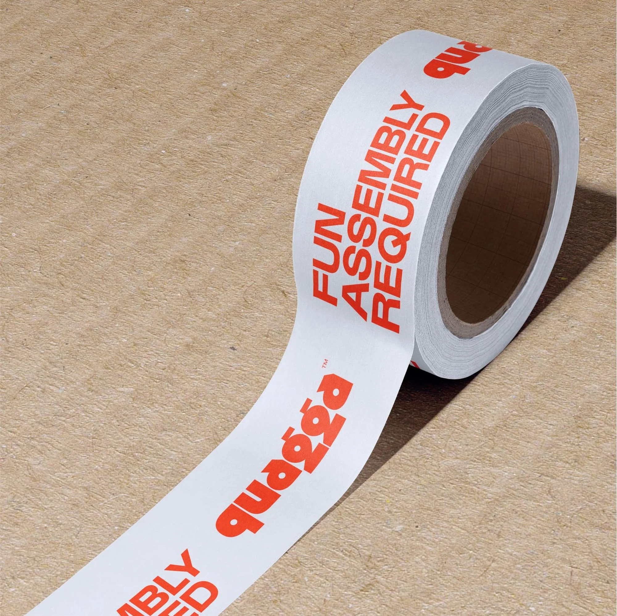 A roll of white tape with the words 'Fun Assembly Required' printed in bold red lettering, sitting on a brown surface.