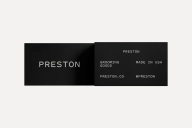 Two black Preston grooming goods business cards laid flat against a pale grey background displaying clean white typography.