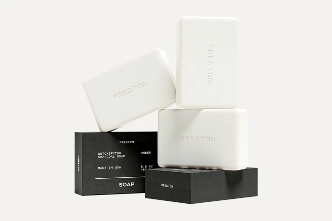 Stacked white soap bars bearing the Preston brand name on dark and light packaging boxes against a solid white background