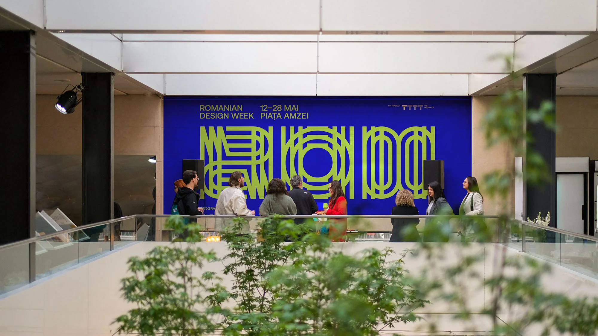 Large group of people congregate on upper level of building with large blue design advertisement during the Romanian Design Week event.