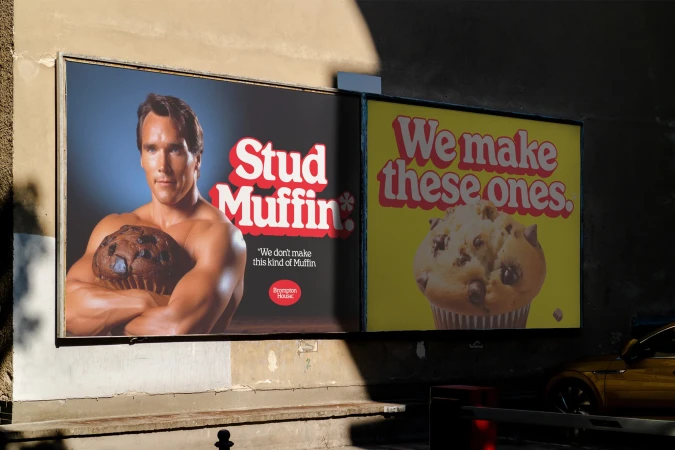 Billboard with bodybuilder holding giant muffin and text 'Stud Muffin'; billboard with muffin and 'We make these ones' text, daytime.