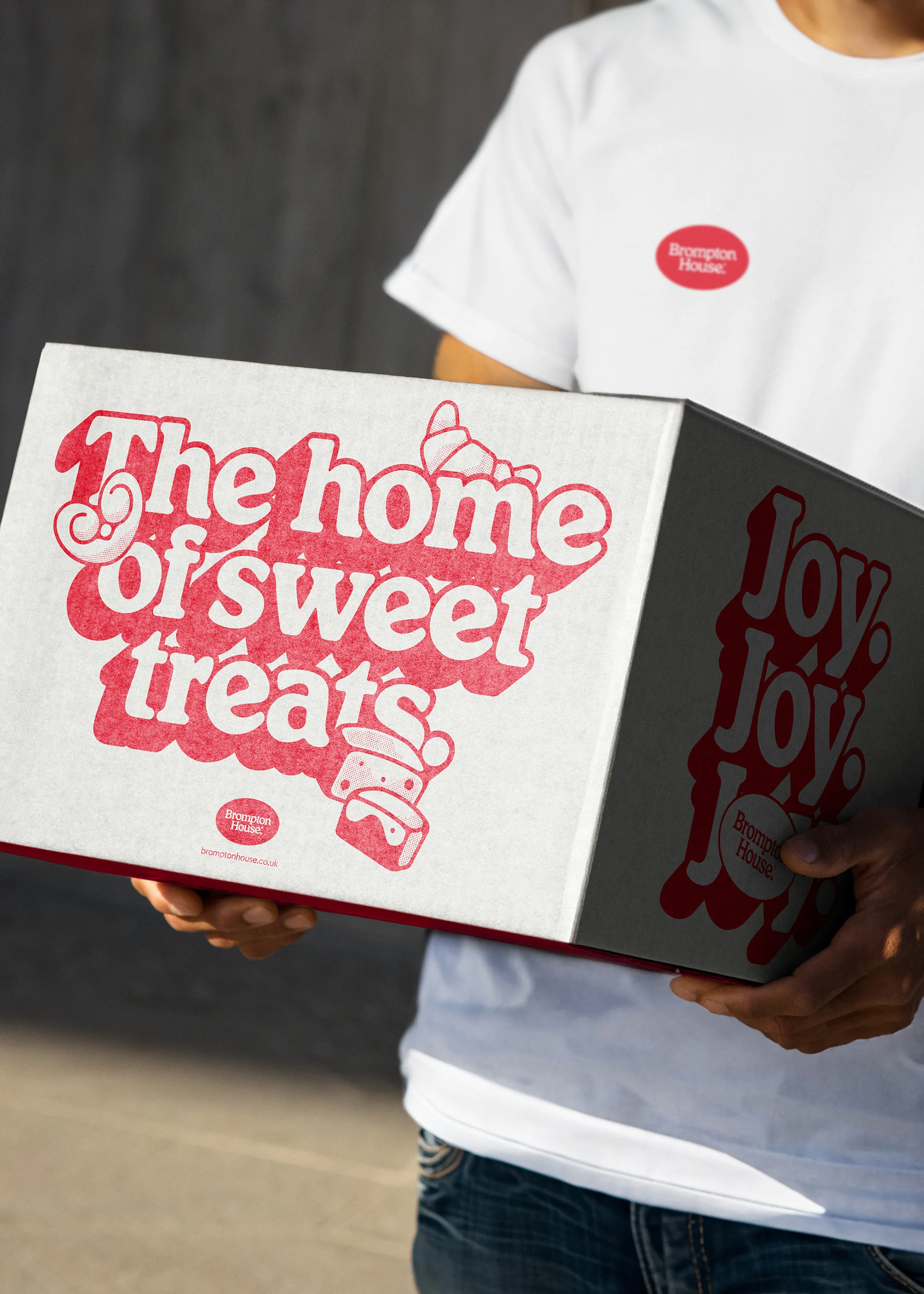 Person in a white t-shirt carries a white cardboard box with the text 'The home of sweet treats' printed in red on the front.