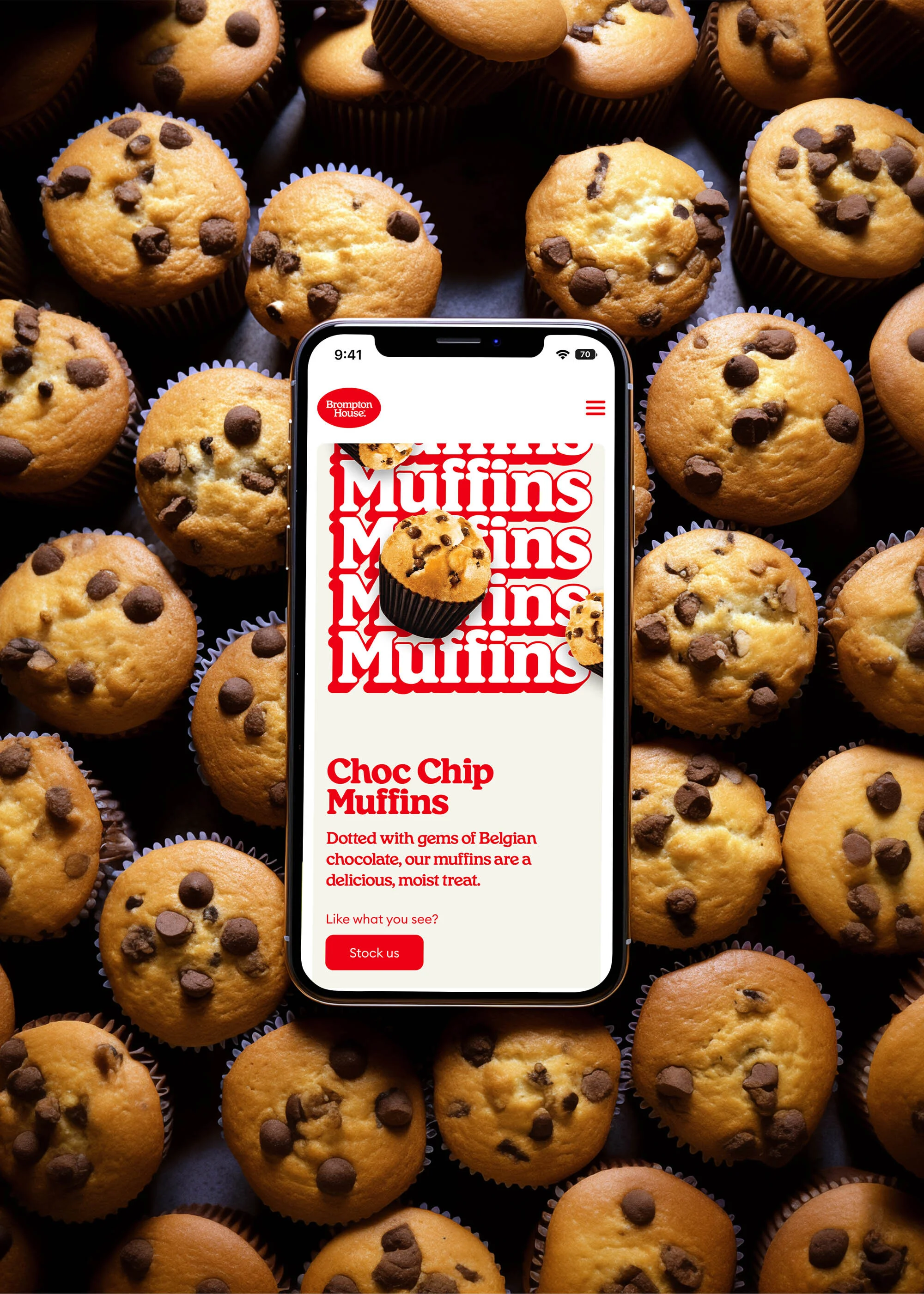 Overhead shot of chocolate chip muffins arranged around a smartphone displaying a muffin advertisement, highlighting food and technology.