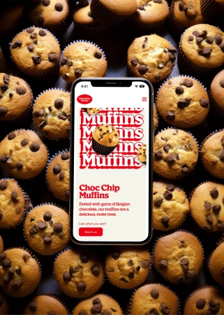 Overhead shot of chocolate chip muffins arranged around a smartphone displaying a muffin advertisement, highlighting food and technology.