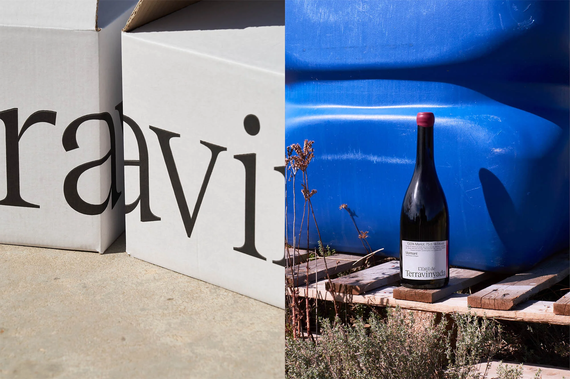 Wine bottle on a wooden pallet next to white branded boxes against a blue background, bright outdoor daylight photography.
