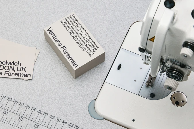 Close-up of sewing machine, ruler, and business cards with 'Ventura Foreman' text on a gray surface.