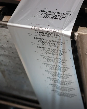 Close-up of a transparent plastic sheet with black text, being processed through an industrial machine in an indoor environment.