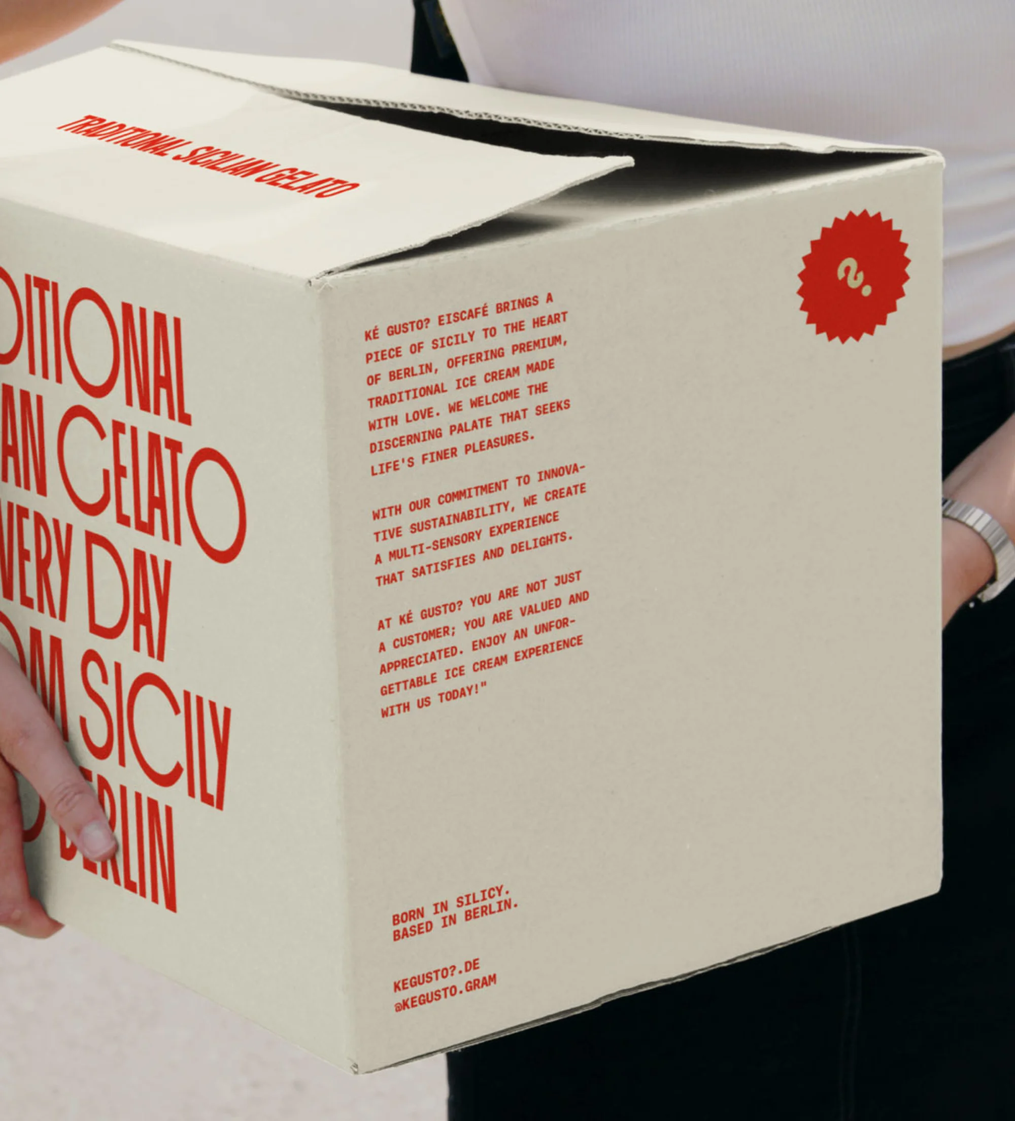 A person holds a branded cardboard box of gelato, with Sicilian gelato text and brand typography in Berlin.