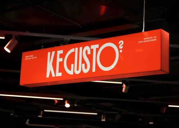 Illuminated orange sign for KE GUSTO? advertises traditional Sicilian gelato with a website and Instagram handle displayed.