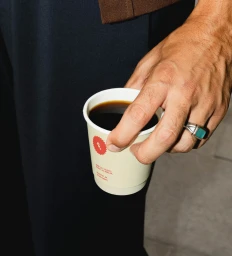 Close-up of a person holding a paper coffee cup with a turquoise signet ring on their hand for Ke Gusto brand identity