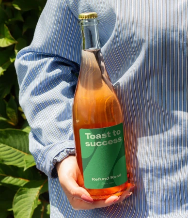 A joyful adult female uses a smartphone inside a home, with soft, natural light and a background featuring plants and neutral decor.