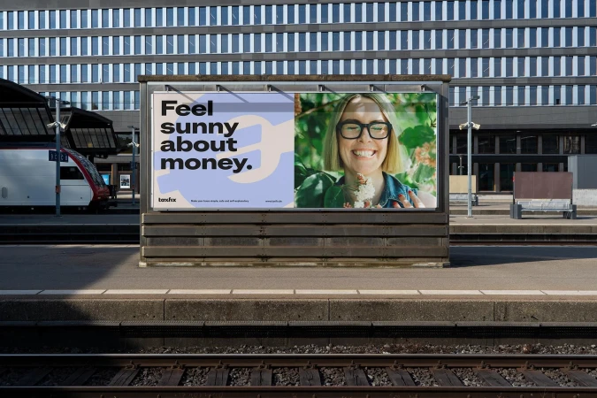 Outdoor advertising billboard featuring a smiling woman in glasses, placed at a train station with a passenger train visible behind.