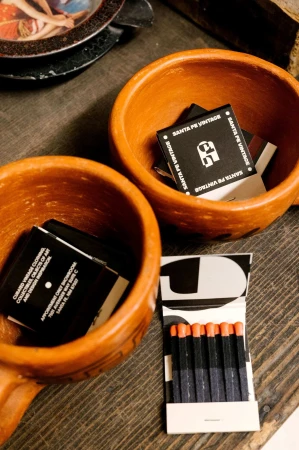 Two terracotta bowls hold matchbooks, with a partially visible matchbook and matches on a rustic wooden surface.