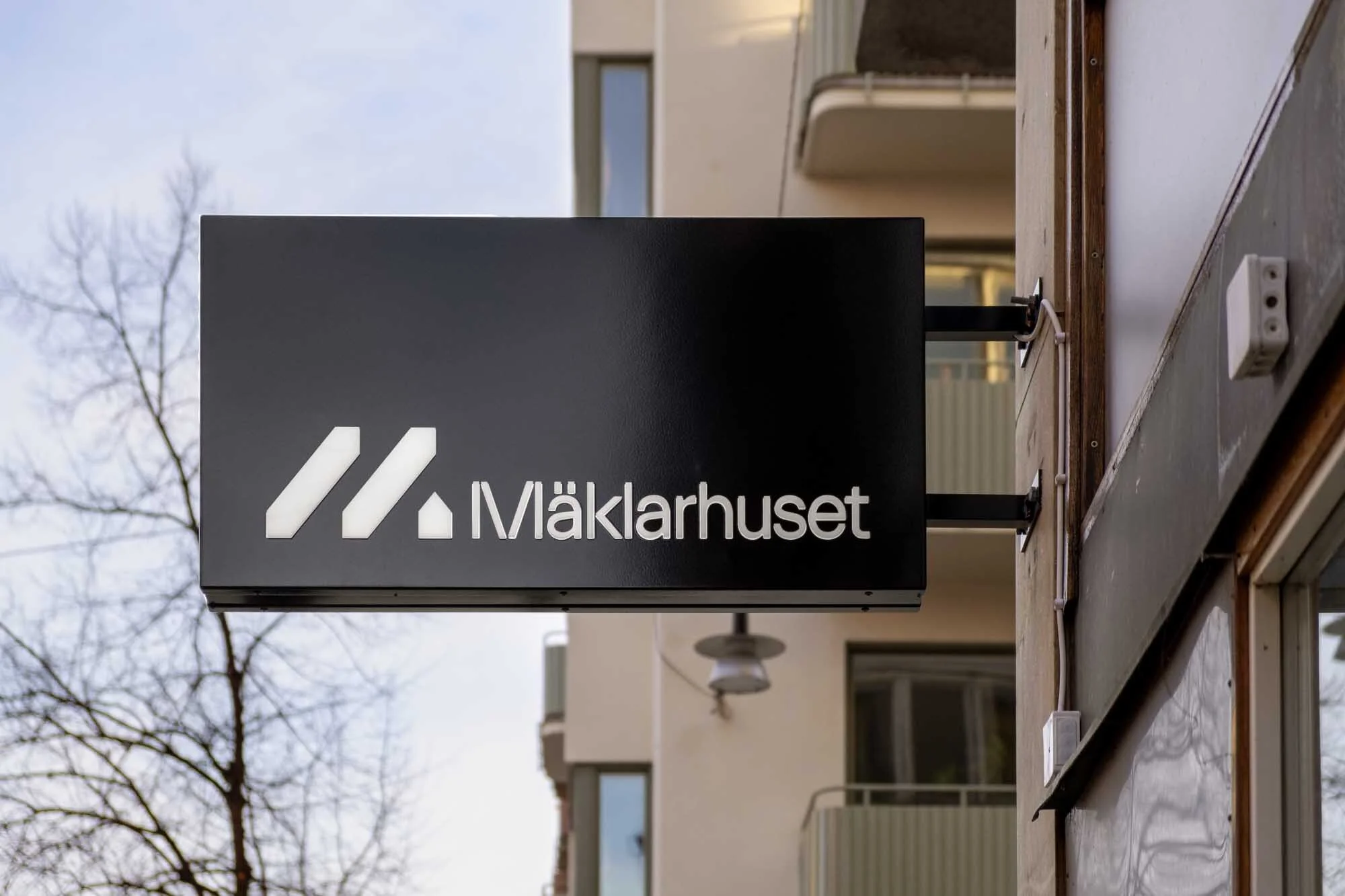 A real estate office sign reading 'Mäklarhuset' in white against a black background on a modern building exterior during daytime.