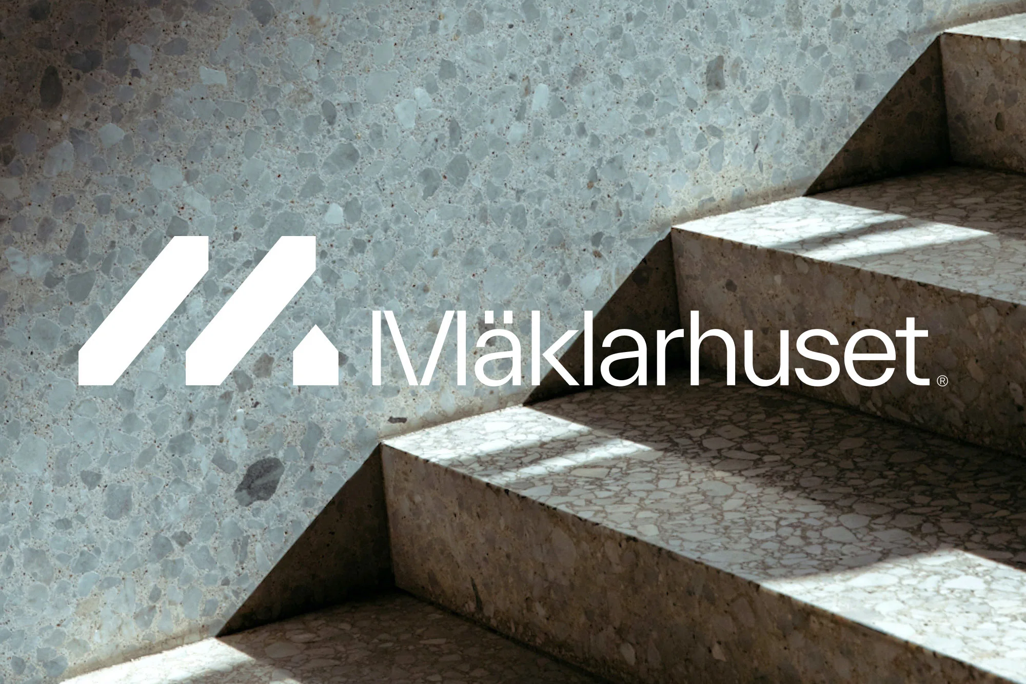Abstract view of a gray terrazzo staircase and wall with the Mäklarhuset logo in white, featuring modern architectural design elements.