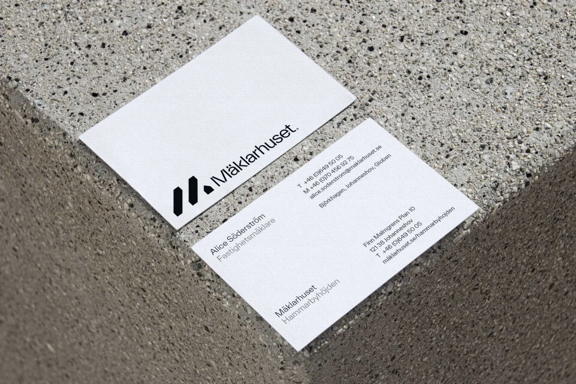 Two white Mäklarhuset business cards on a textured gray stone surface, minimalist design with contact details and logo.