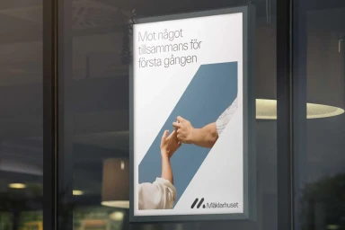 An illuminated advertising poster mounted on a storefront window displaying Swedish text and two hands touching against a blue and white graphic background.