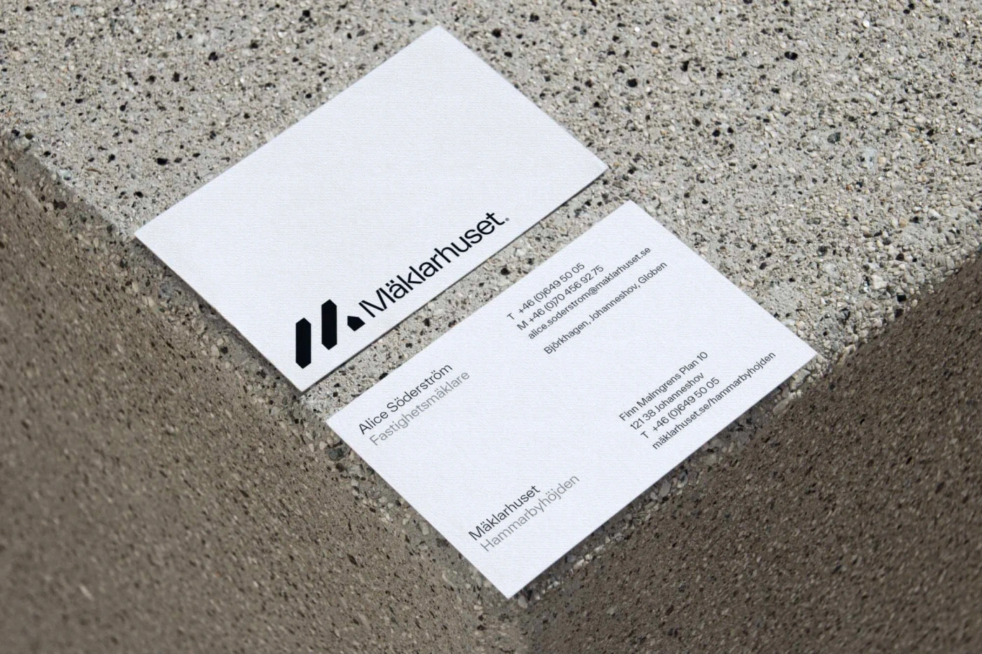 Two white business cards with black typography resting on a textured grey stone surface.